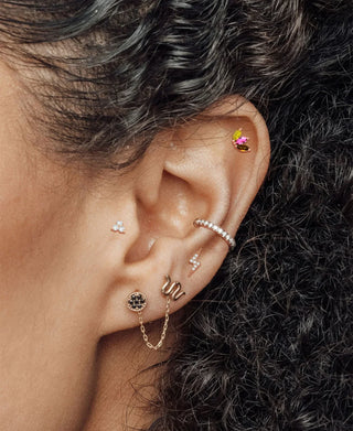 Ear-styling reference with a dark round lobe stud, small decorative accents and a linking chain