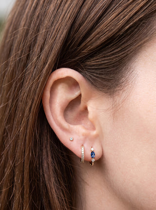 Diana 10mm yellow gold huggies with blue sapphire and lab-grown diamonds worn on an ear.