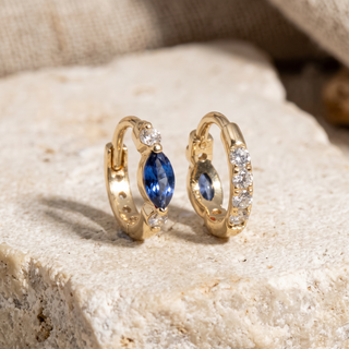 14K yellow gold huggie hoop earrings featuring a marquise-cut blue sapphire accented by round white diamonds, paired with a diamond-set gold hoop design.