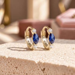 Diana 10mm 14K yellow gold huggies with marquise blue sapphires between round lab-grown diamonds on a stone display.