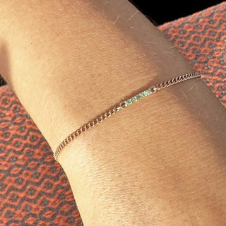 A delicate silver chain bracelet with a single emerald-green gemstone book permanent jewelry in denver nina wynn appointment