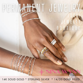 Hand wearing multiple pieces of permanent jewelry and engagement rings with 'Nina Wynn' branding