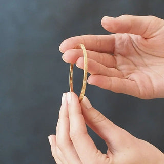 A delicate gold 14k bangle with a subtle textured pattern from the vortex diamond gold collection held between fingers