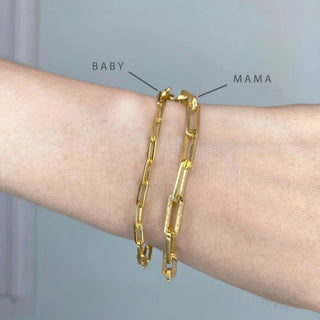 Two gold-toned paperclip 14k yellow gold bracelets labeled baby and mama worn together on wrist