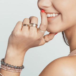 A woman’s hand wearing multiple rose gold rings alongside a black diamond 14k white gold ring