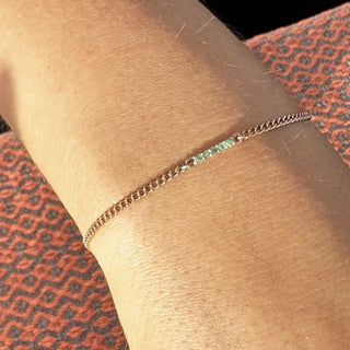 A delicate silver chain bracelet with a single emerald-green gemstone book permanent jewelry in denver nina wynn appointment