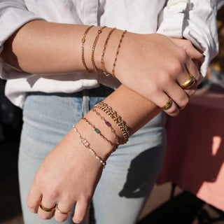 A collection of gold-toned permanent jewelry bracelets with gemstone accents worn on wrists during a nina wynn appointment in denver
