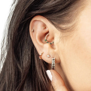 A delicate gold-toned hoop earring with green gemstones and a diamond accent for ear piercing denver by nina wynn