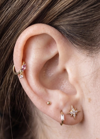 Cartilage hoop earrings in 14k gold featuring a radiant pink sapphire and dangling charm. Feminine luxurious statement