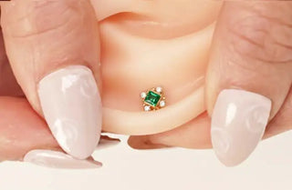 A delicate gold nose ring featuring a square-cut emerald surrounded by four small diamonds.