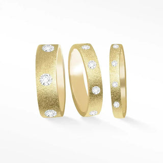 Three gold diamond cigar band rings with textured surfaces and round diamonds set along the sides in 14k gold