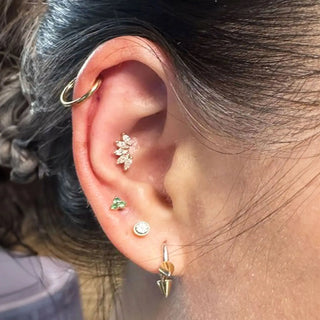A gold-toned leaf-shaped earring with clear stones and a green gemstone by nina wynn for ear spa denver