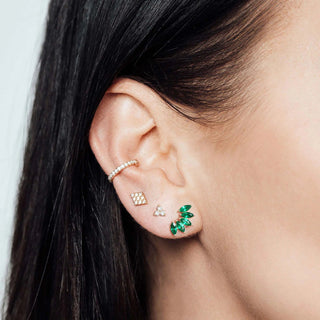 A delicate gold-toned ear cuff with sparkling clear stones paired with 14k lotus flat back emerald stud earrings
