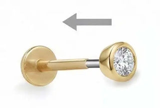 Gold-colored labret piercing with a round, clear gemstone set in the front and a flat back plate.