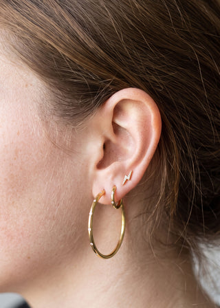 Gold hoop earrings with delicate diamond accents paired with a small gold lightning bolt stud, styled together on an ear for an elegant, layered look.