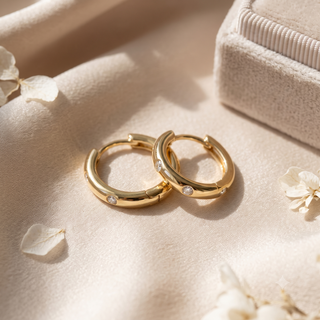 14K yellow gold diamond hoop earrings featuring polished huggie hoops with sparkling round diamonds, displayed on beige fabric in warm natural lighting.