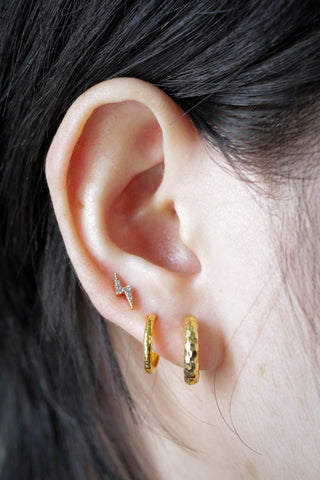 Gold lightning bolt stud earring with tiny sparkling stones complementing hammered gold hoop earrings style