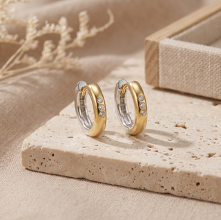 Pair of two-tone gold hoops displayed upright on a stone surface