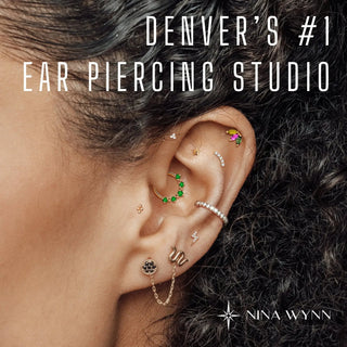 A person’s ear showcasing a bespoke jewelry experience gift with gold and silver piercings featuring green gemstone and diamond cuffs