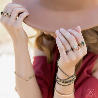 A woman’s hand with nina wynn 14k yellow gold rings featuring green and pink gemstones at a jewelry shopping appointment