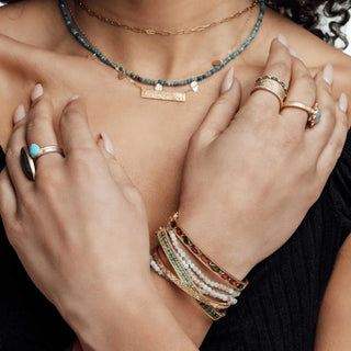 A stack of gold-toned bangles with colorful gemstones and white beads for a Nina Wynn jewelry shopping appointment