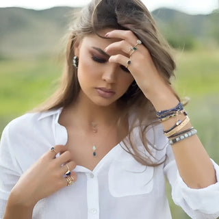A woman wearing a white shirt showcasing nina wynn 14k yellow gold convertible earrings and multiple gold bracelets