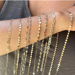 Permanent jewelry training in Seattle: gold-tone chain and gemstone connector styles arranged across a forearm.