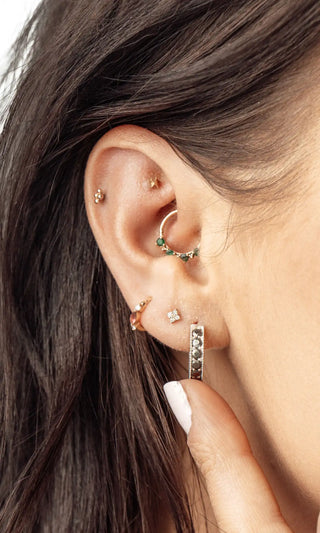 A silver hoop earring adorned with green gemstones and a small diamond accent.