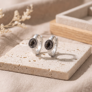 Element Mini geode silver hoops with dark crystal centers on a stone display