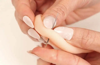 A delicate, flesh-toned silicone finger puppet being gently held between fingers with a thin metal needle.