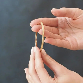 A delicate gold 14k bangle with a subtle textured pattern from the vortex diamond gold collection held between fingers