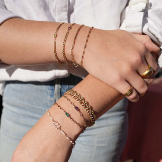 Assorted chain bracelets with colorful gemstone accents layered on both wrists.
